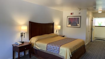 A hotel room with a large bed, two bedside lamps, a telephone, a painting on the wall, and a door leading to another room.