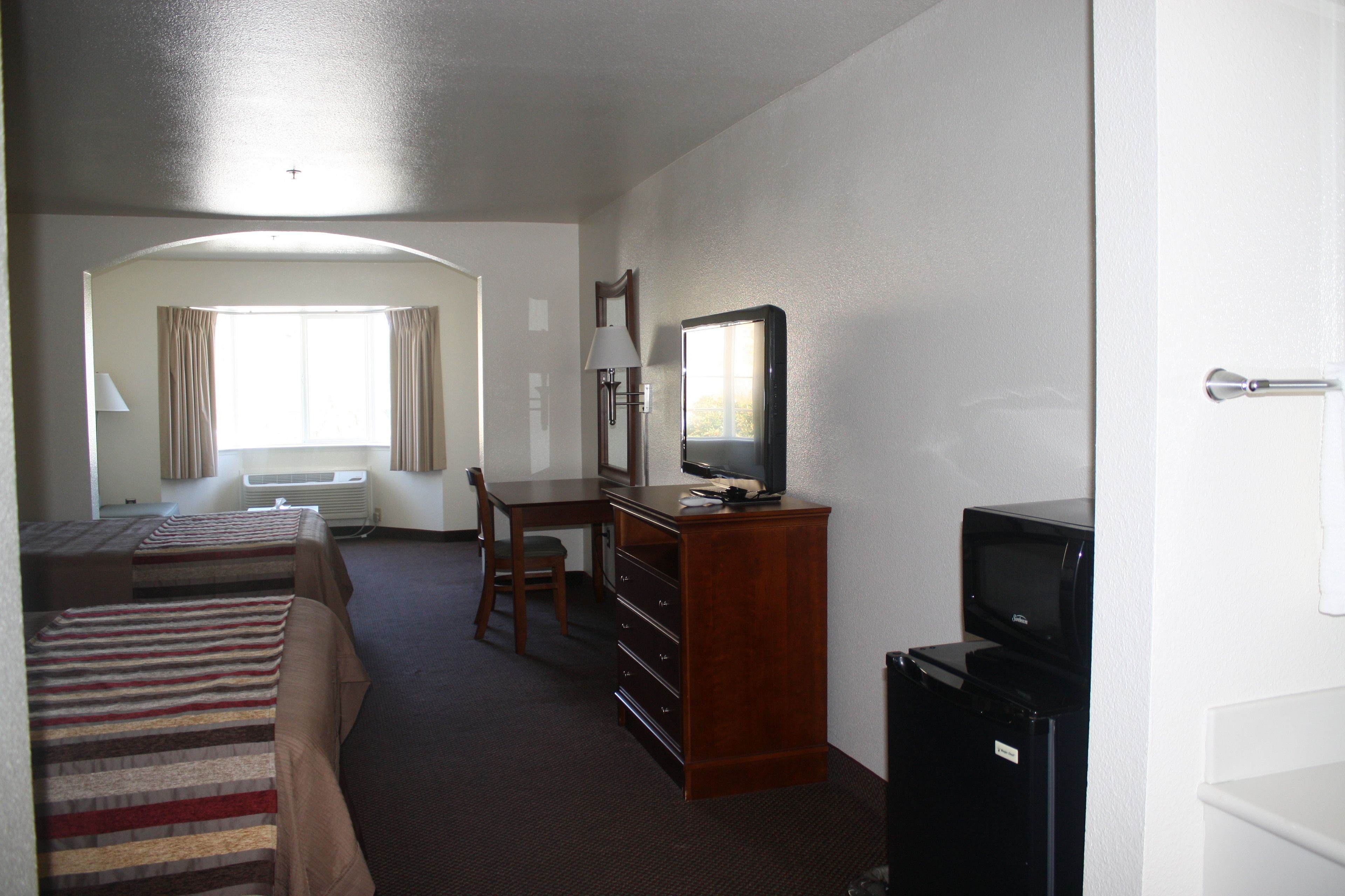 Een hotelkamer met twee bedden, een bureau, een televisie en een koelkast.