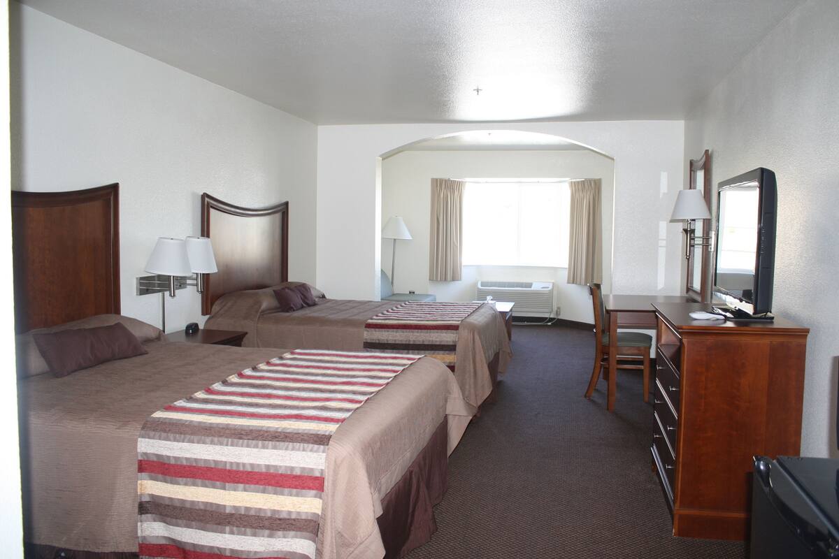 A hotel room with three beds, a desk, a chair, a television, and a window with curtains.