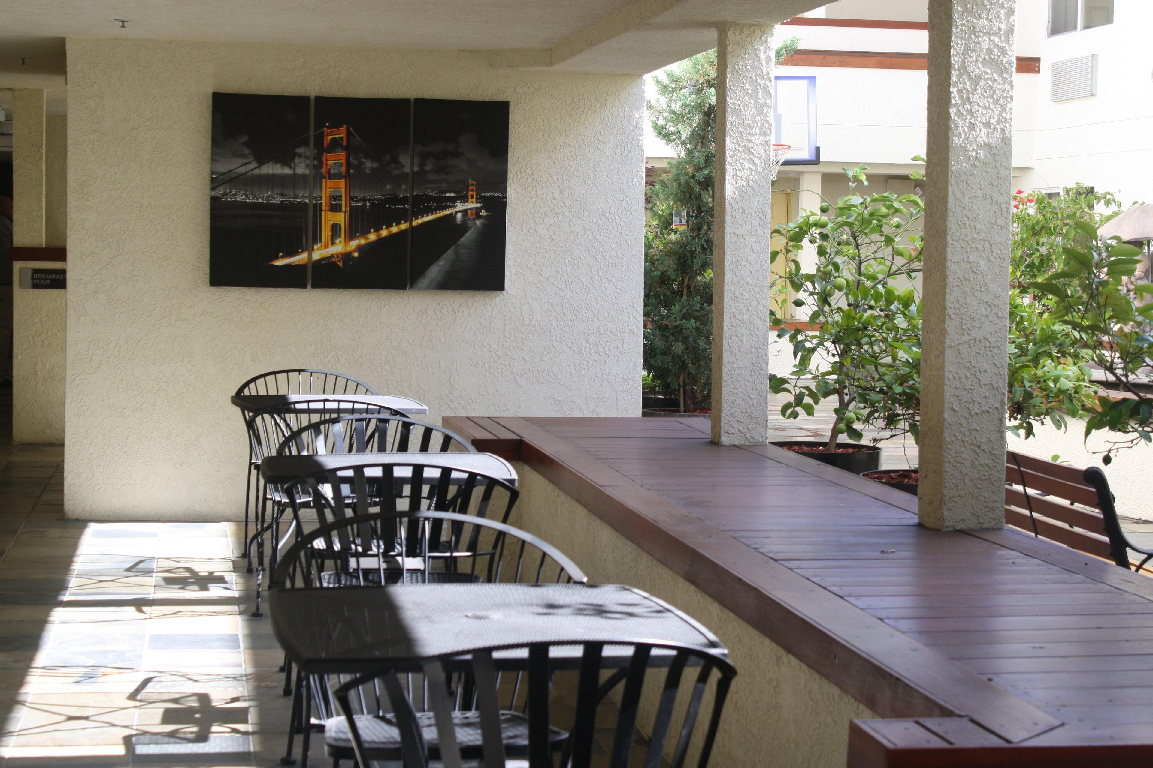 A covered outdoor seating area with tables and chairs, a view of a cityscape with a bridge, and potted plants.