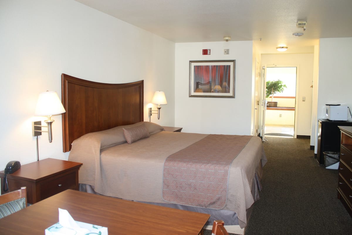 A hotel room with a large bed, bedside lamps, a desk with a telephone, and a framed picture on the wall.