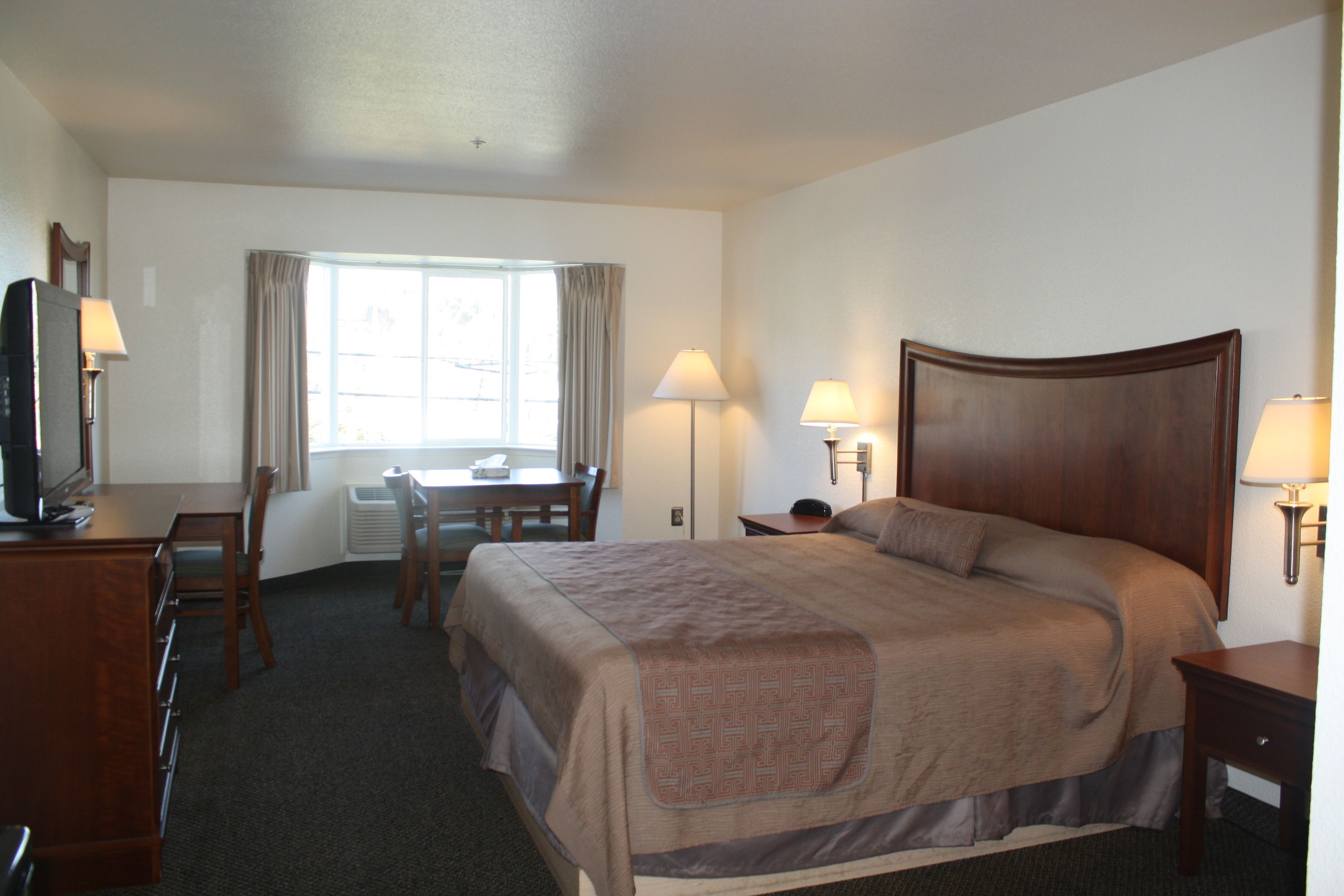 A hotel room with a large bed, a desk, a chair, a television, and two lamps.