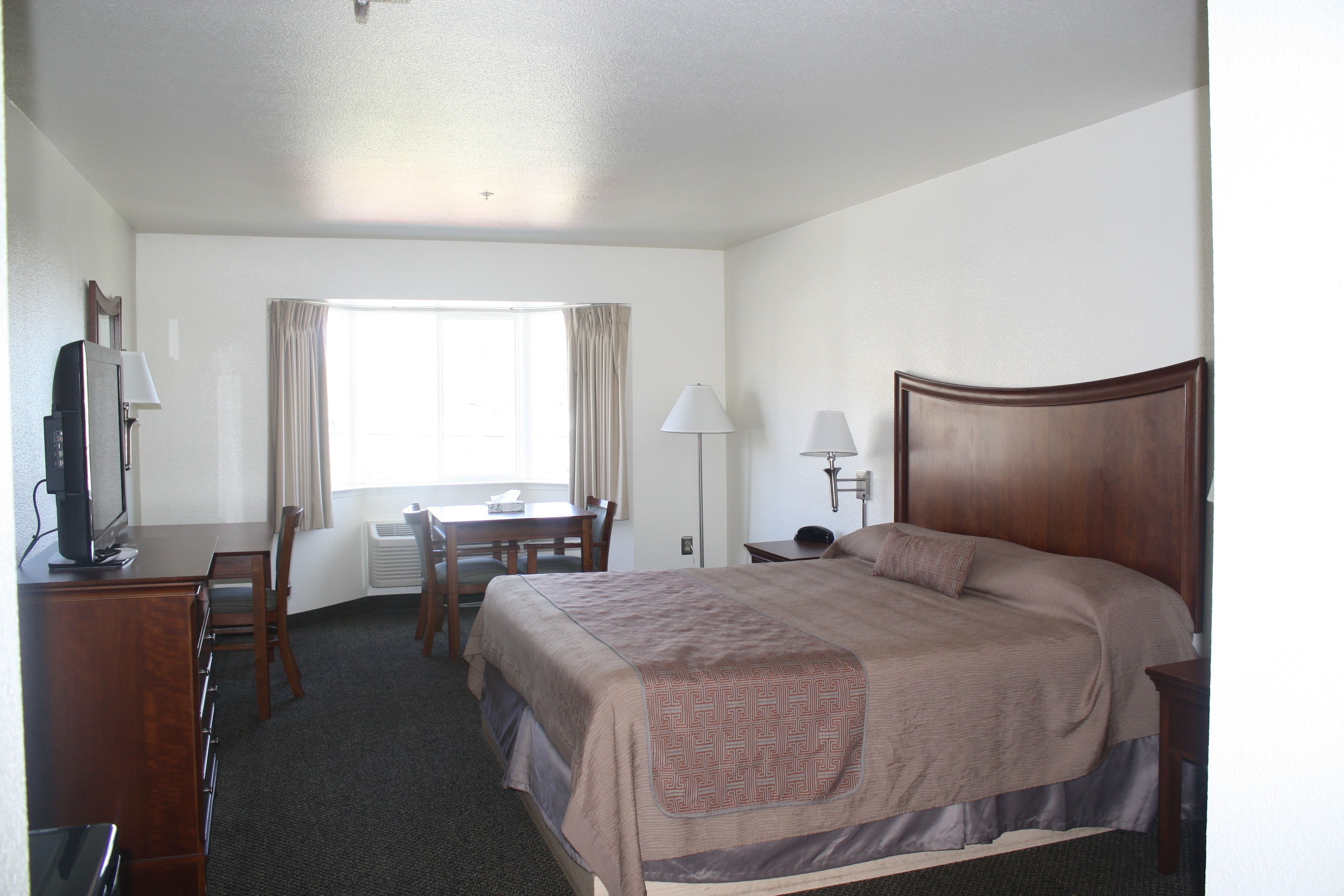 A hotel room with a bed, desk, chair, lamp, and a television.