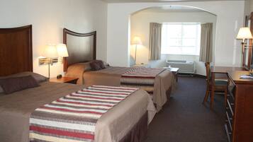 A hotel room with two beds, a desk, a chair, a lamp, and an air conditioning unit.