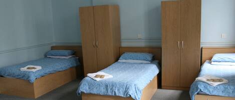 Una habitación con tres camas de madera, cada una con colcha y almohadas azules, y dos armarios de madera grandes.