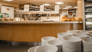 Une cuisine professionnelle équipée d’appareils en acier inoxydable, un buffet garni de différents plats et une horloge au mur.