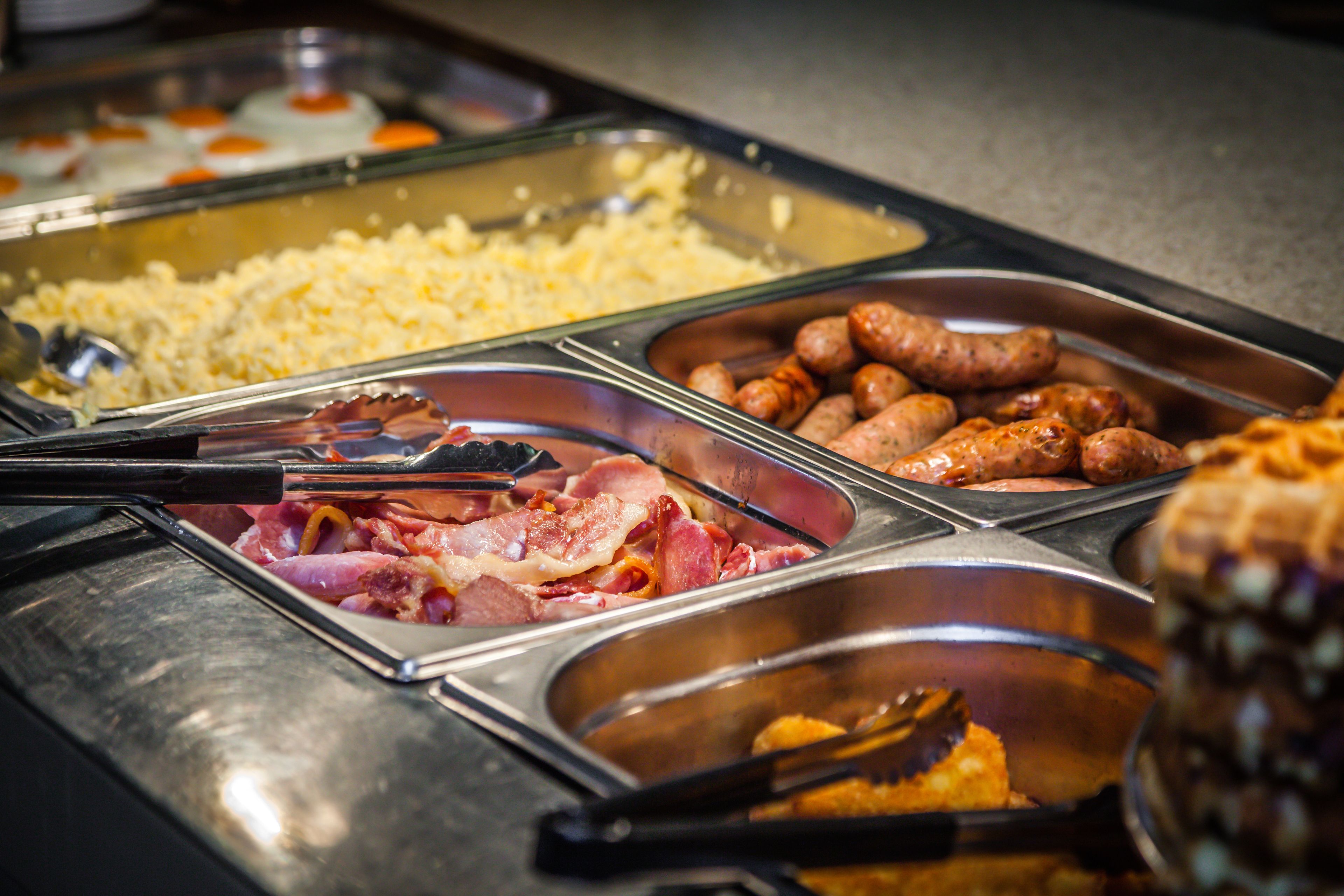 A buffet with various food items including sausages, bacon, and scrambled eggs.
