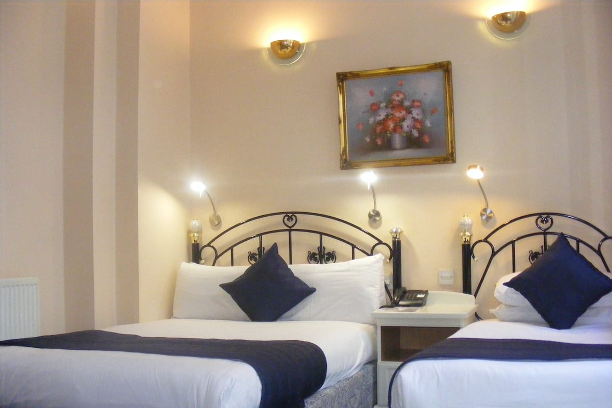 A hotel room with two beds, each with a headboard, a bedside table, and a lamp. There is a painting on the wall above the beds.