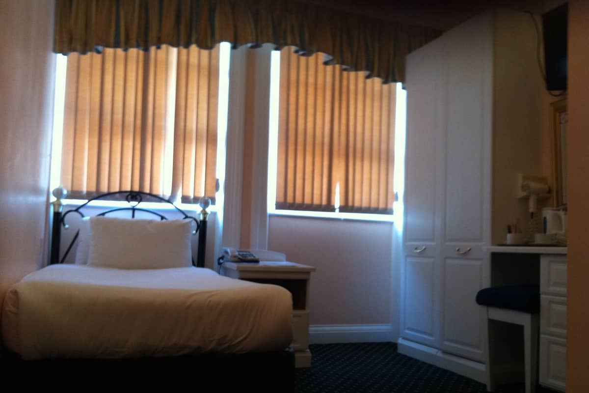 A hotel room with a bed, bedside table, lamp, and a small desk with a chair.