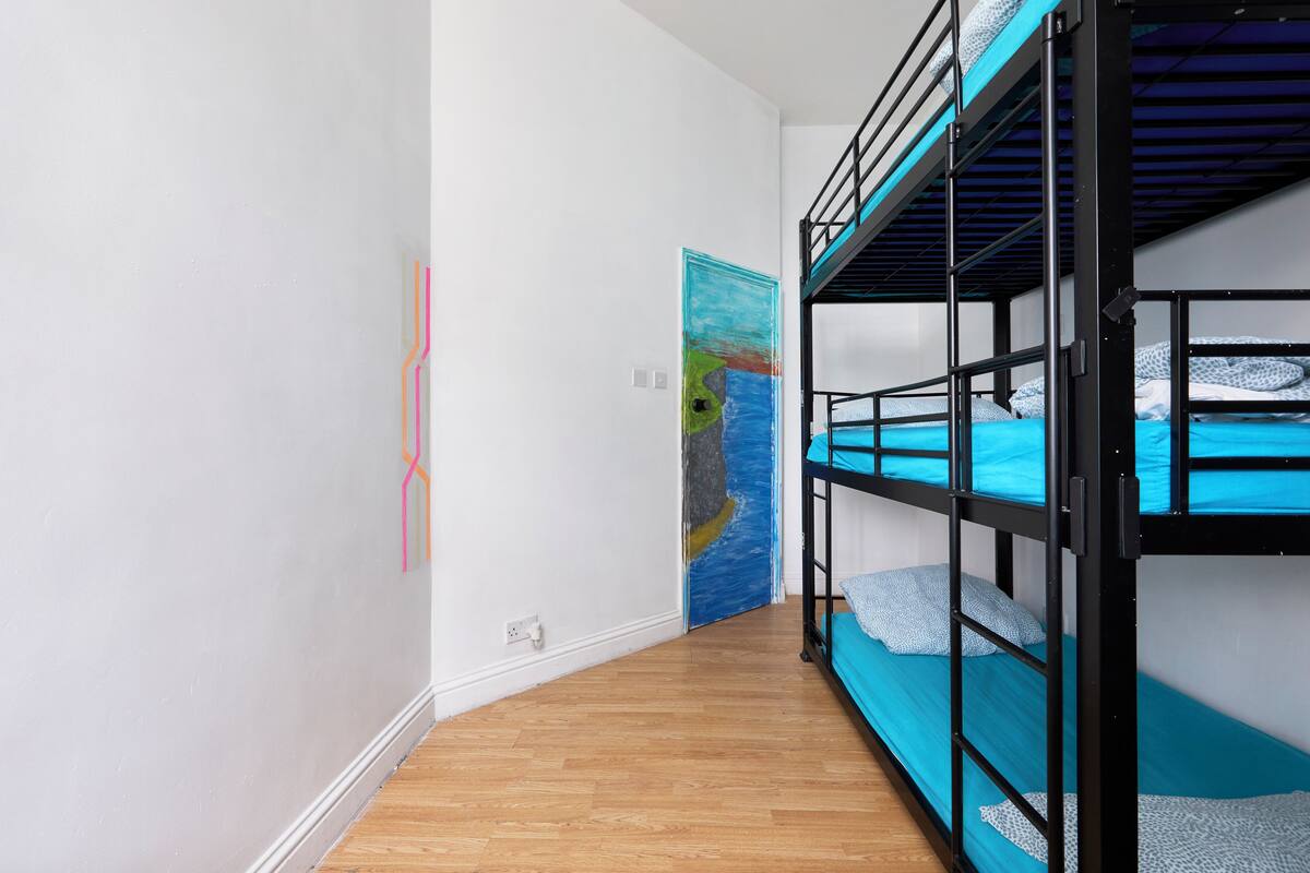 A room with bunk beds, wooden flooring, and a colorful abstract painting on the wall.