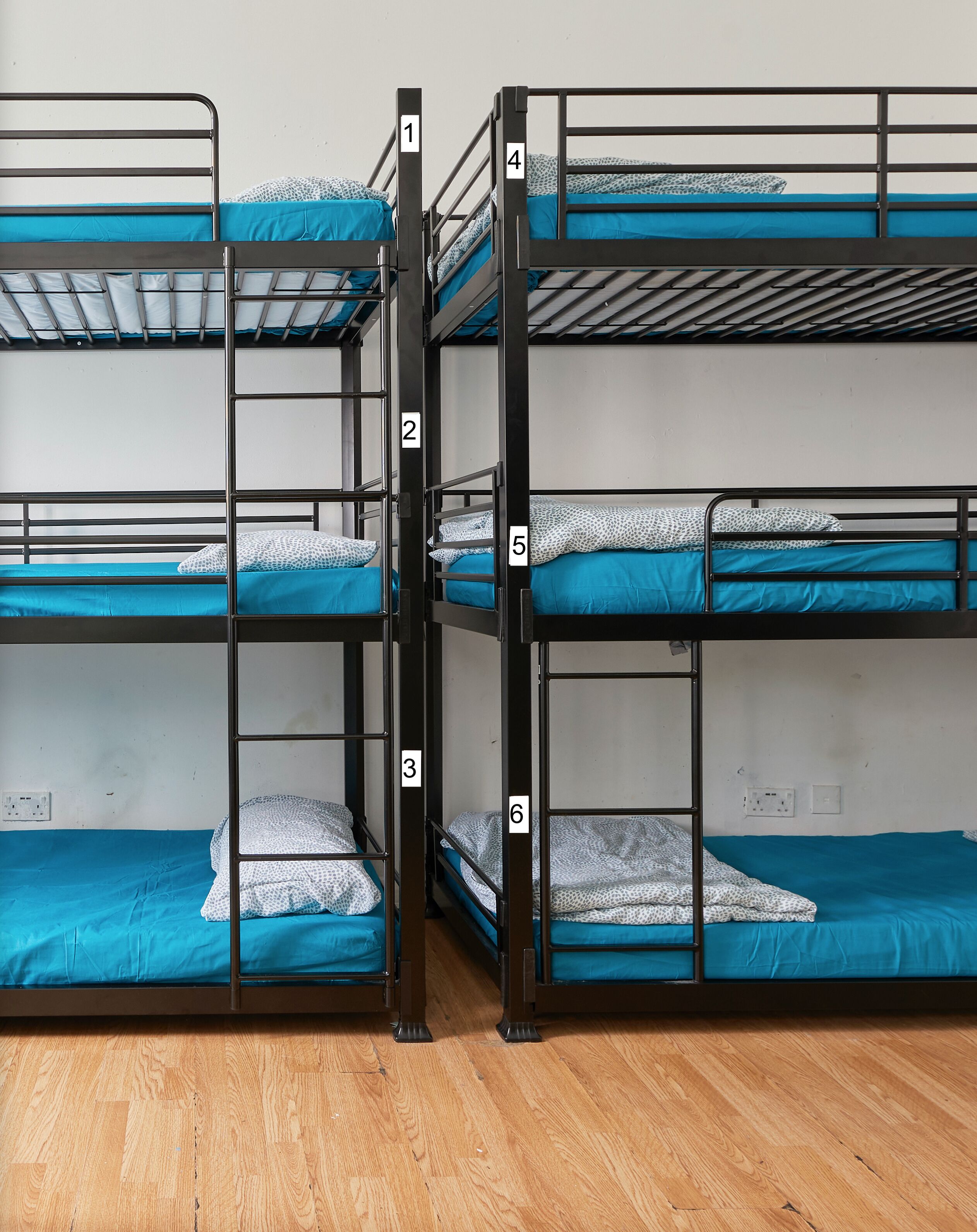 A bunk bed room with three bunk beds, each with a blue mattress and white patterned pillows.