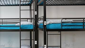 Quarto com beliches, três no total, cada um com colchão azul e almofadas estampadas brancas.