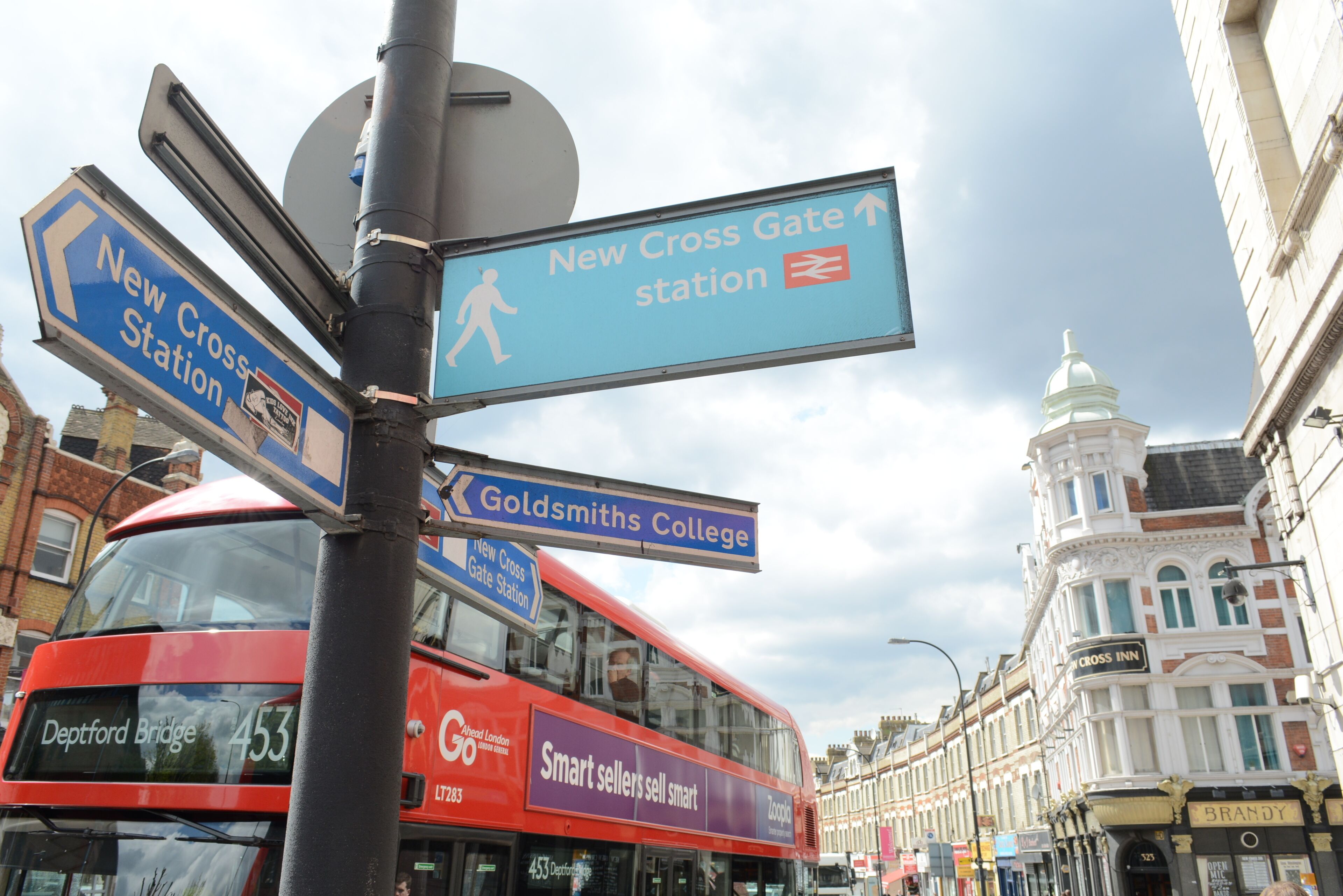 A street sign with directions to New Cross Station and Goldsmiths College.