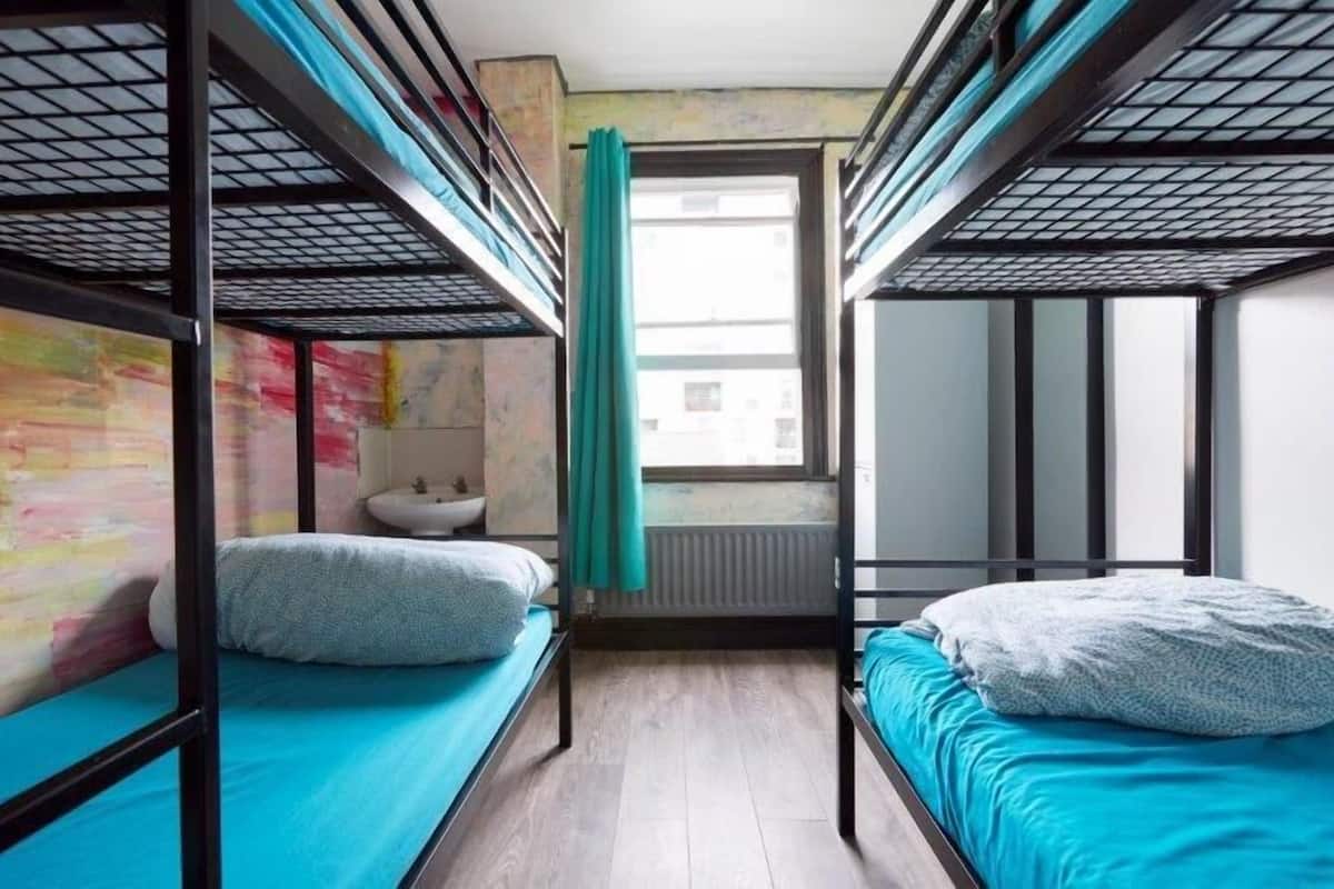 A dormitory room with bunk beds, a window with a curtain, a sink, and a radiator.