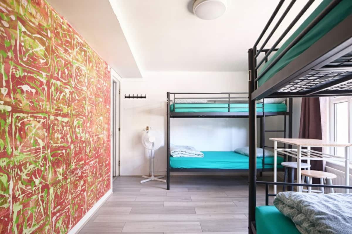 A room with bunk beds, a fan, a table, and a colorful abstract wall.