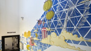 Un mural amb una noria, núvols i un edifici.