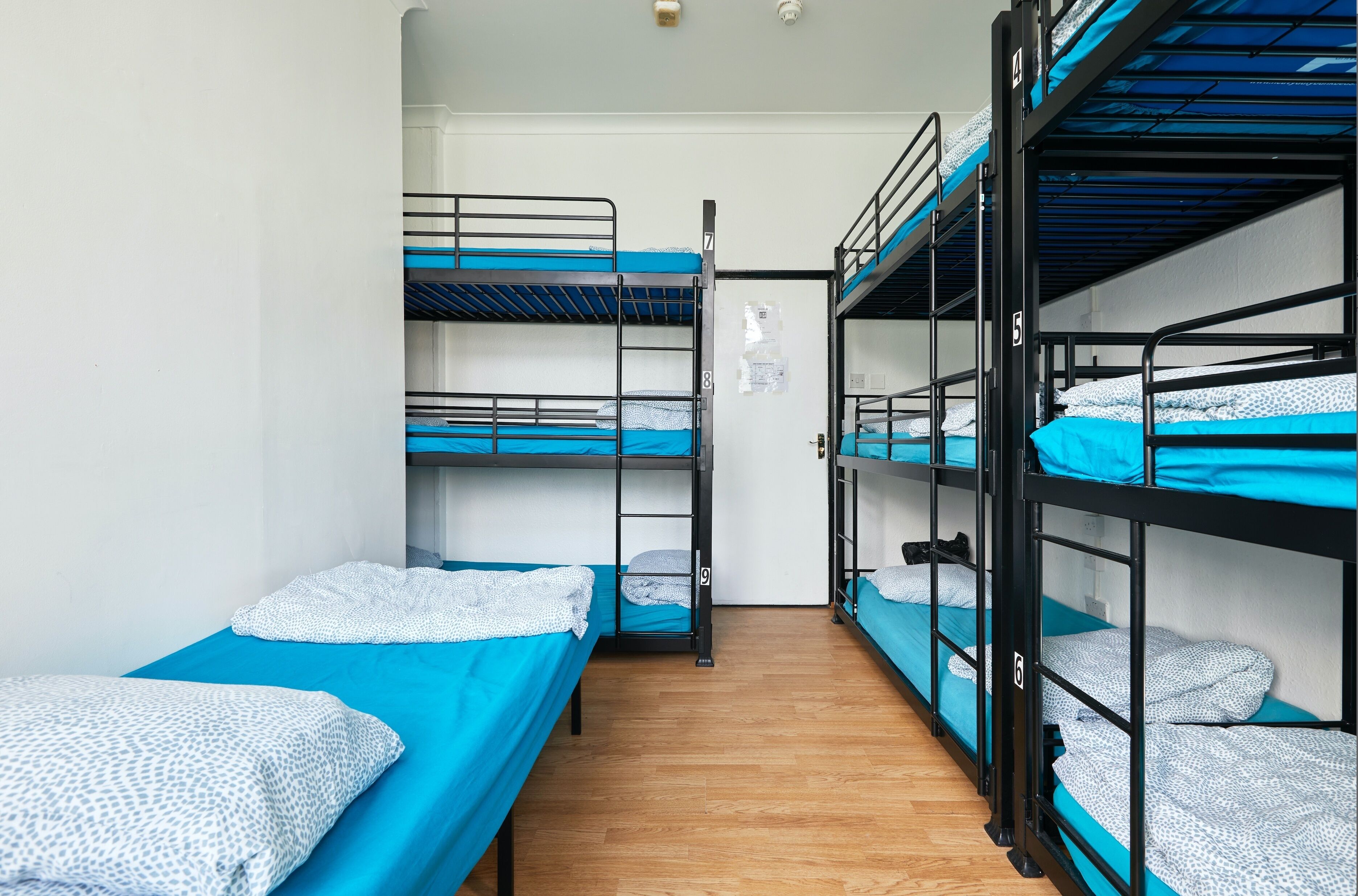 A dormitory room with bunk beds, wooden flooring, and a white door.