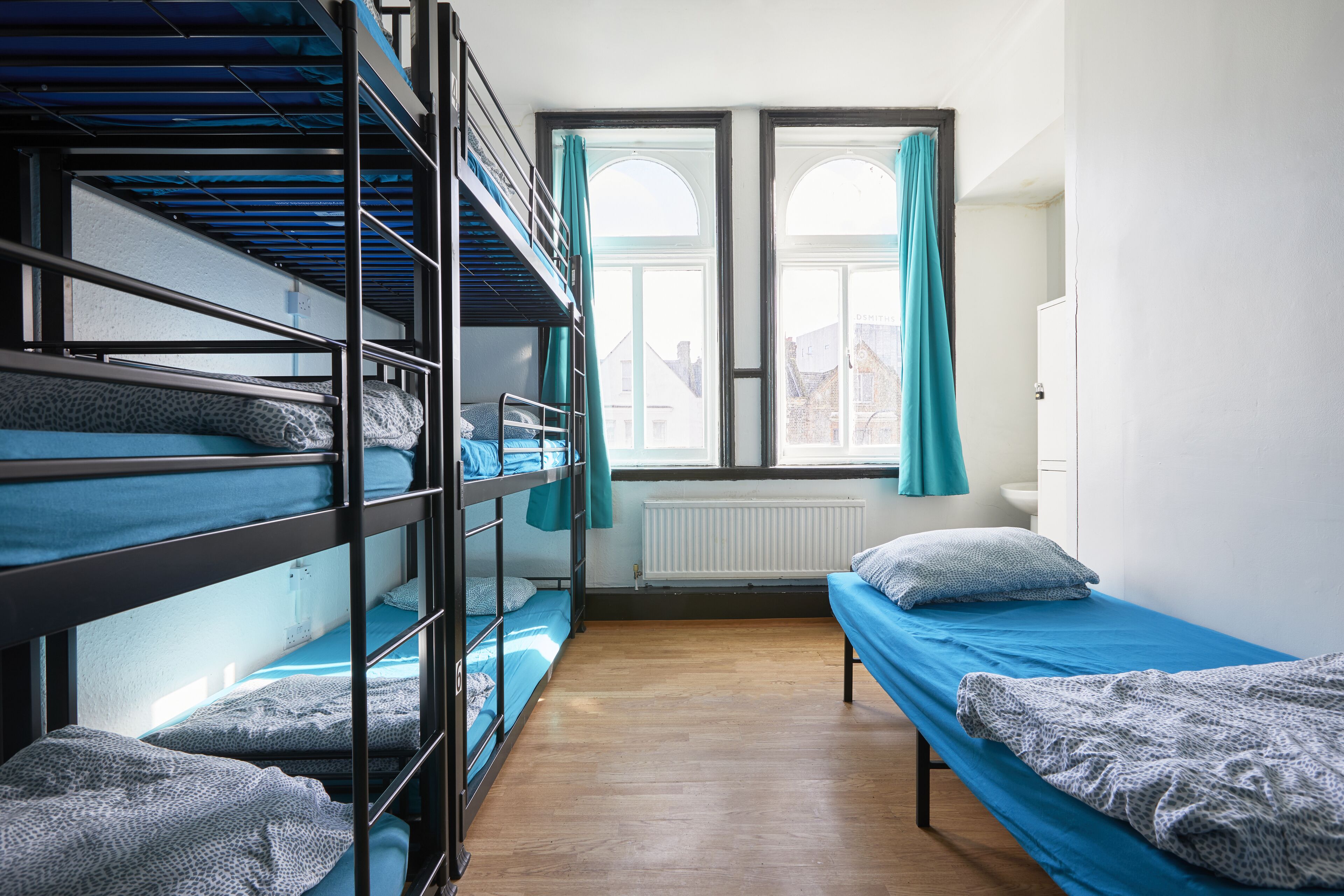 Ein Schlafsaal mit Etagenbetten, einem Einzelbett, einem Fenster mit Vorhängen und einem Heizkörper.