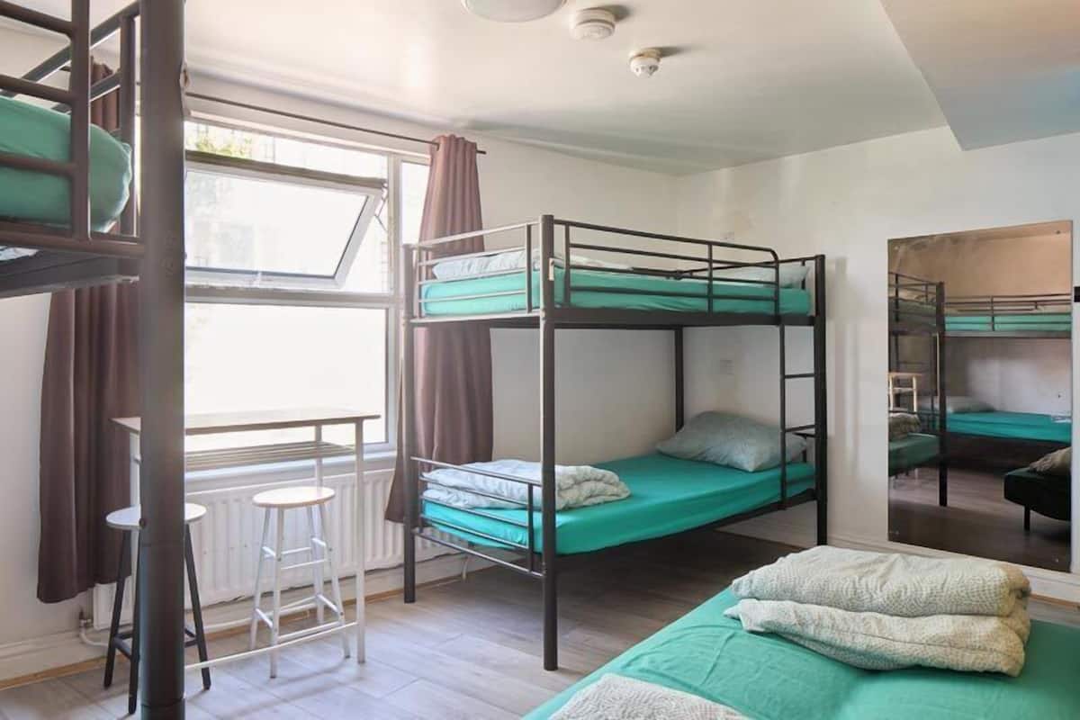 A dormitory room with bunk beds, a window with curtains, and a radiator.