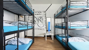 Una habitació de dormitori amb llits superposats, una taula blanca i una paret amb art abstracte.