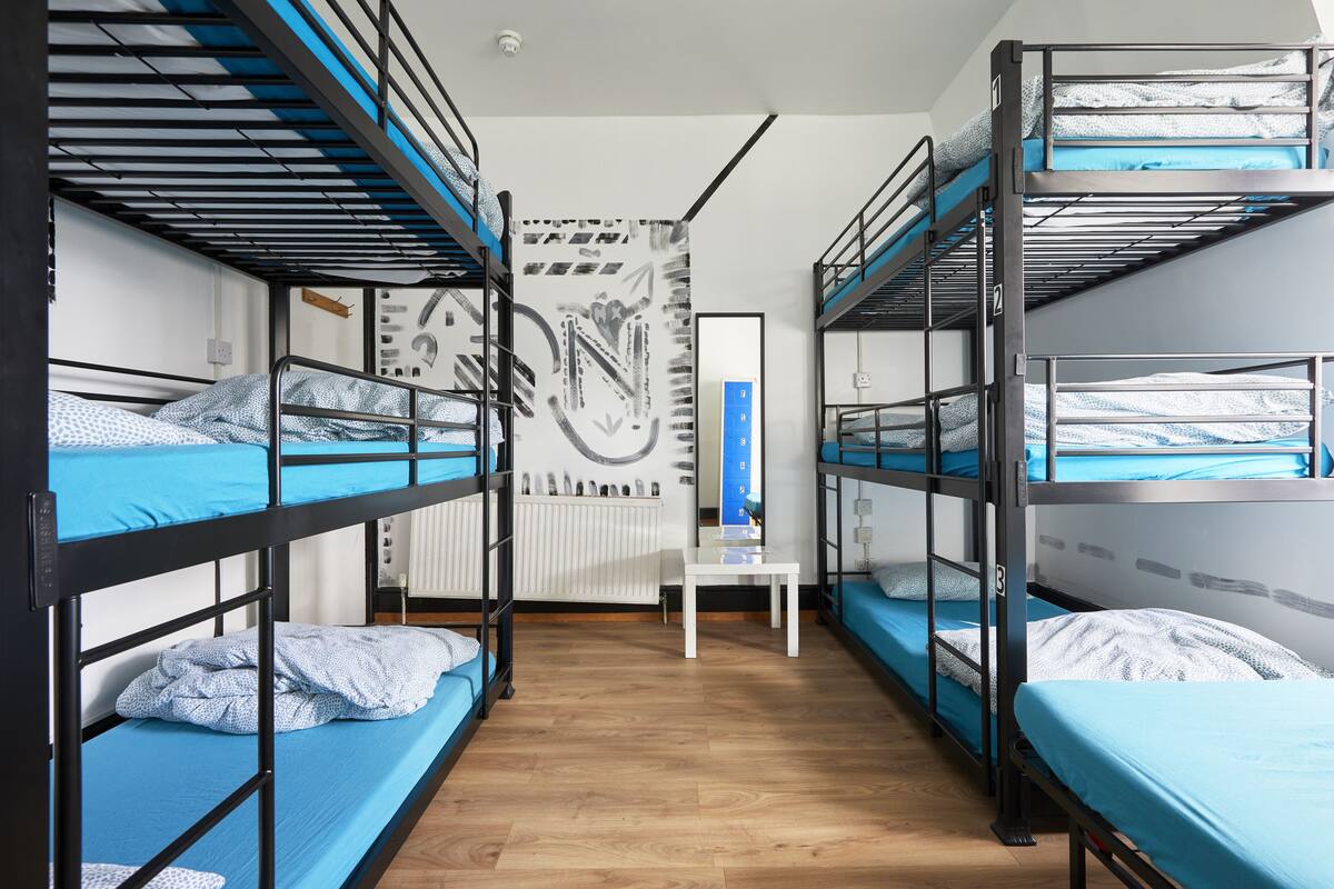 A dormitory room with bunk beds, a white table, and a wall with abstract art.