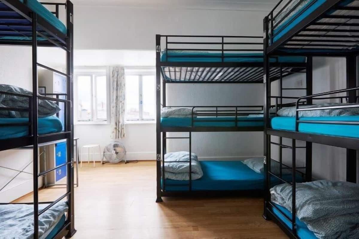 A dormitory room with bunk beds, a fan, and a window with curtains.