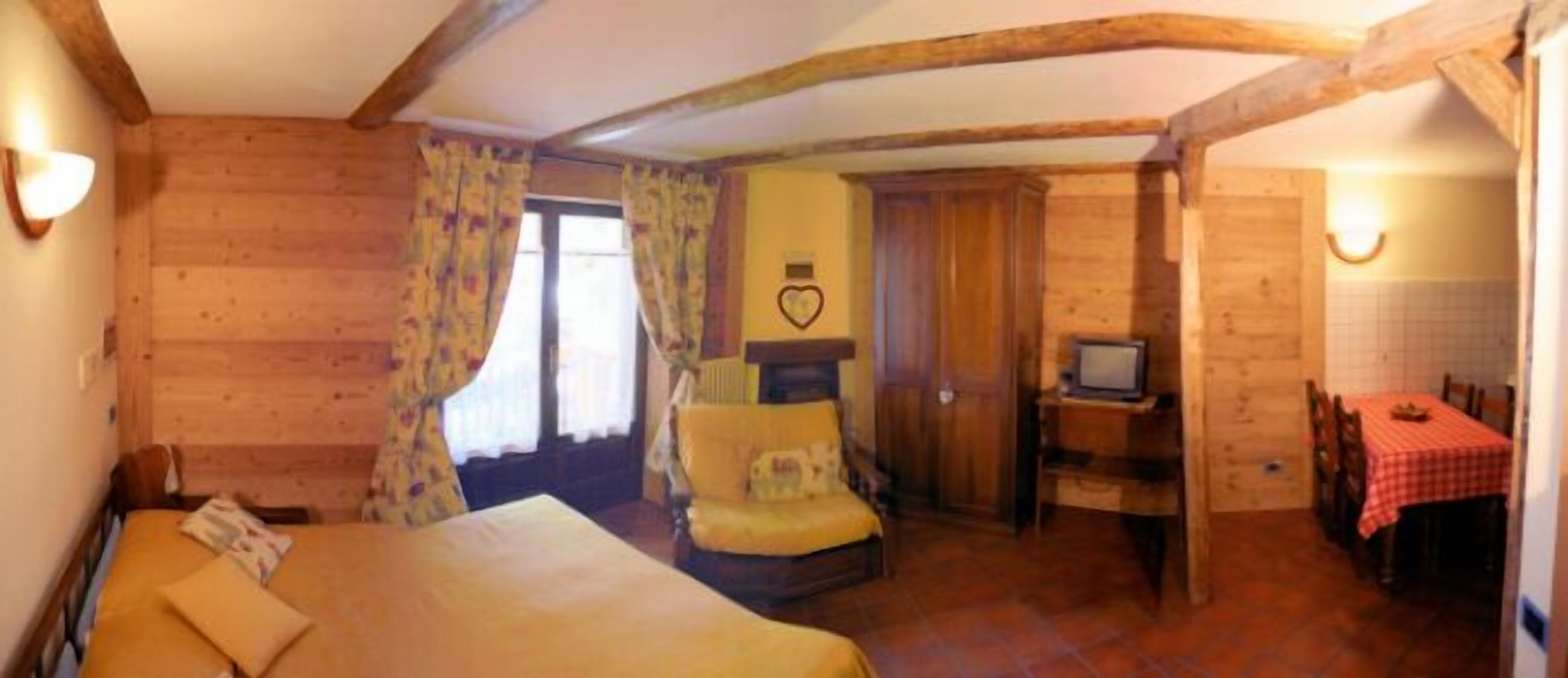 A cozy room with a bed, a chair, a small table with a television, and a dining table with a red checkered tablecloth.