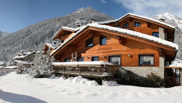 A wooden chalet with a balcony, surrounded by snow-covered trees and mountains.