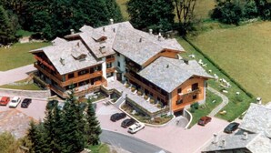 A large, multi-story building with a stone roof, surrounded by trees and a parking area.