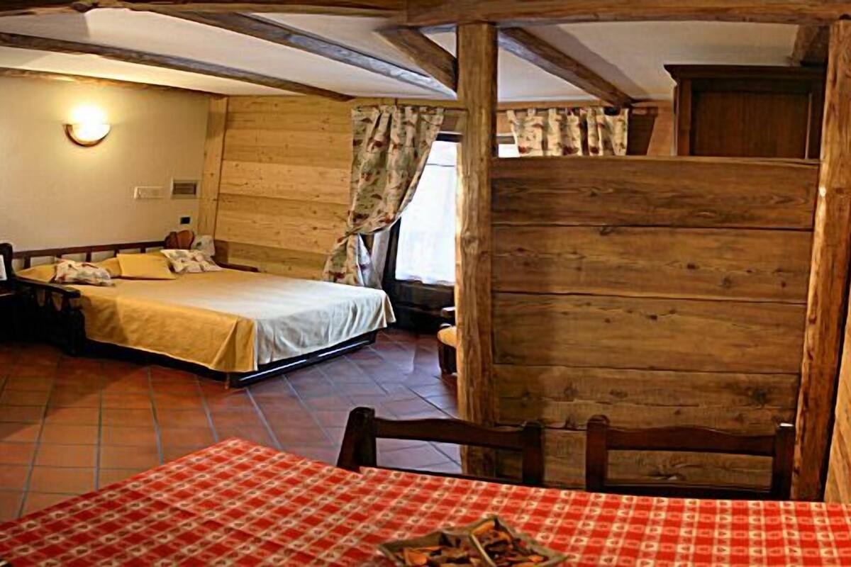 A rustic wooden room with a bed, a table with a checkered tablecloth, and a chair.