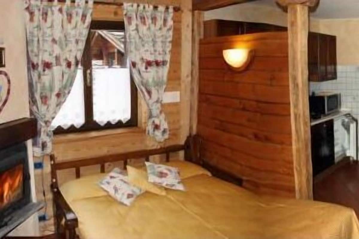 A cozy room with a bed, a fireplace, a dining table with chairs, and a kitchen area.