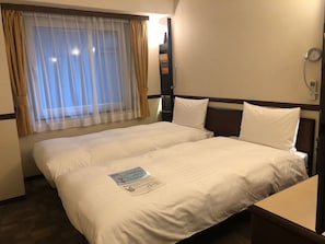 A hotel room with two beds, a window with sheer curtains, a bedside table, and a wall clock.