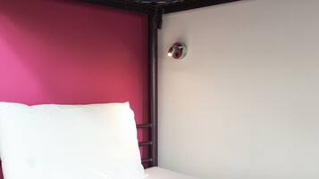 A single bed with a white mattress and a white pillow in a room with a red wall and a white ceiling.
