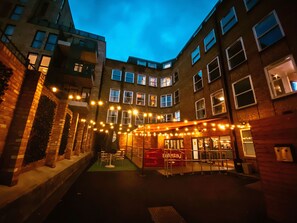 A courtyard with string lights, a red sign, and a building with multiple windows. - Safestay London Elephant & Castle (London)