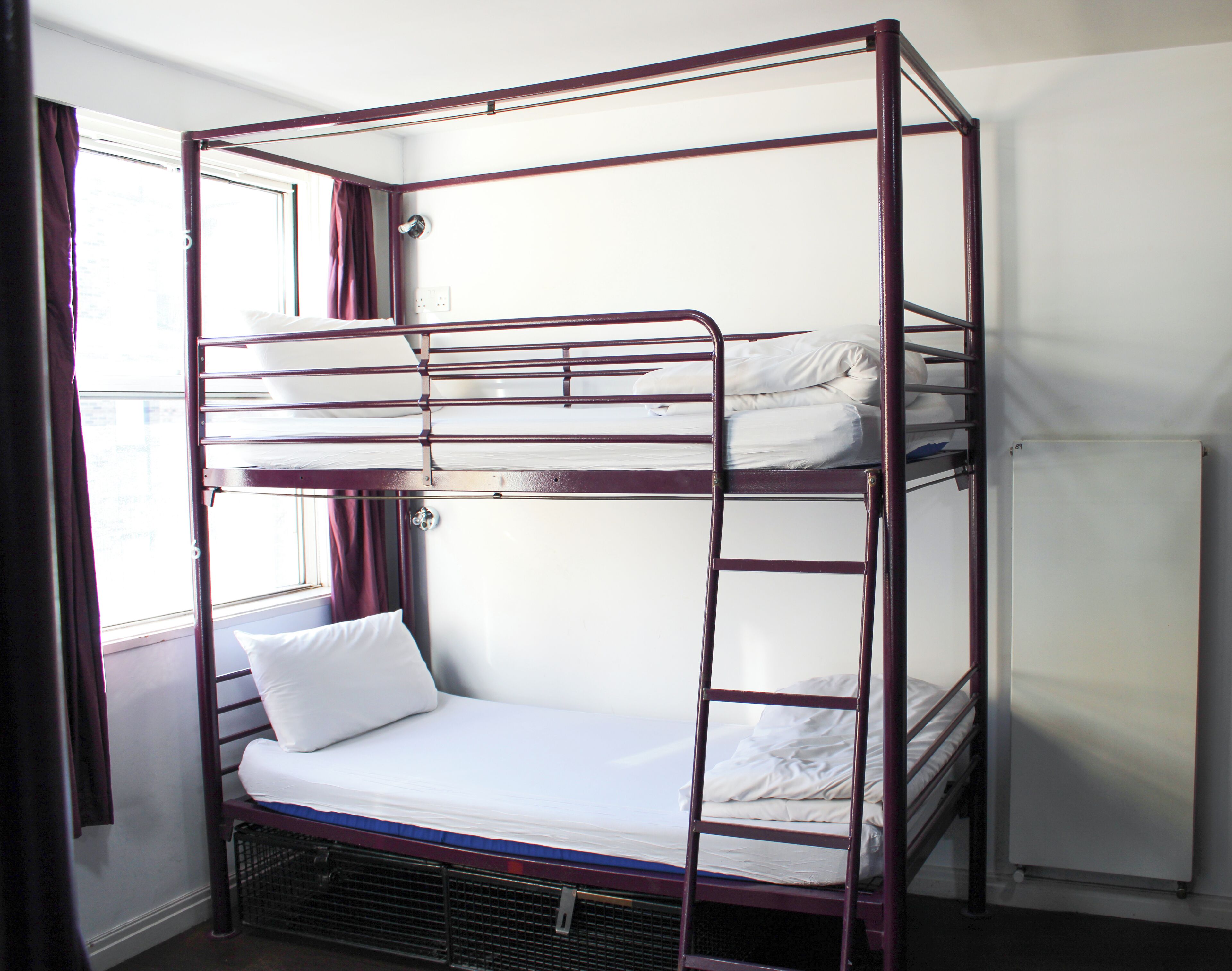 A bunk bed with a ladder, a window with curtains, and a radiator.