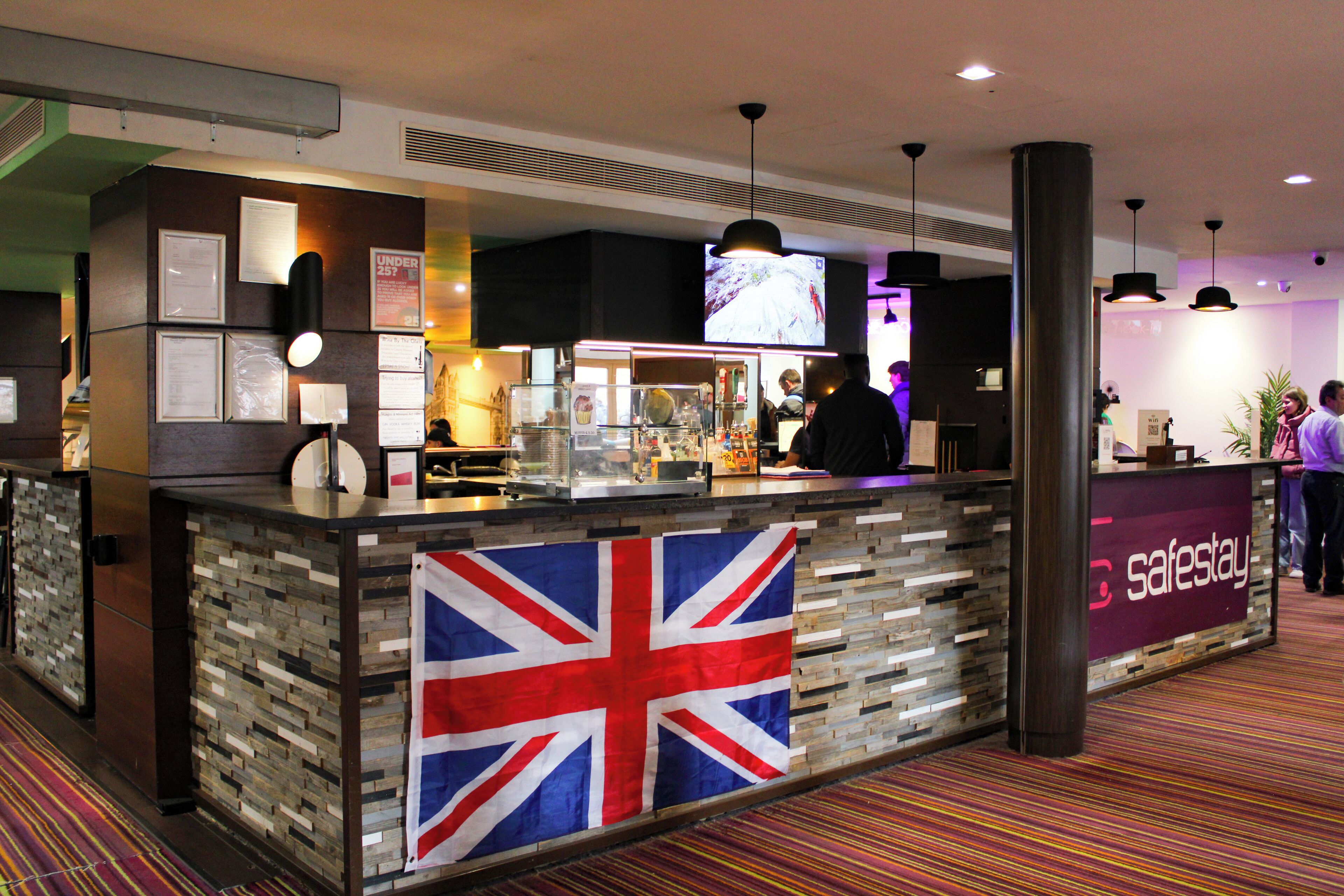 A reception desk with a Union Jack flag, a 'safestay' sign, and a television screen above.