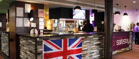 A reception desk with a Union Jack flag, a 'safestay' sign, and a television screen above.