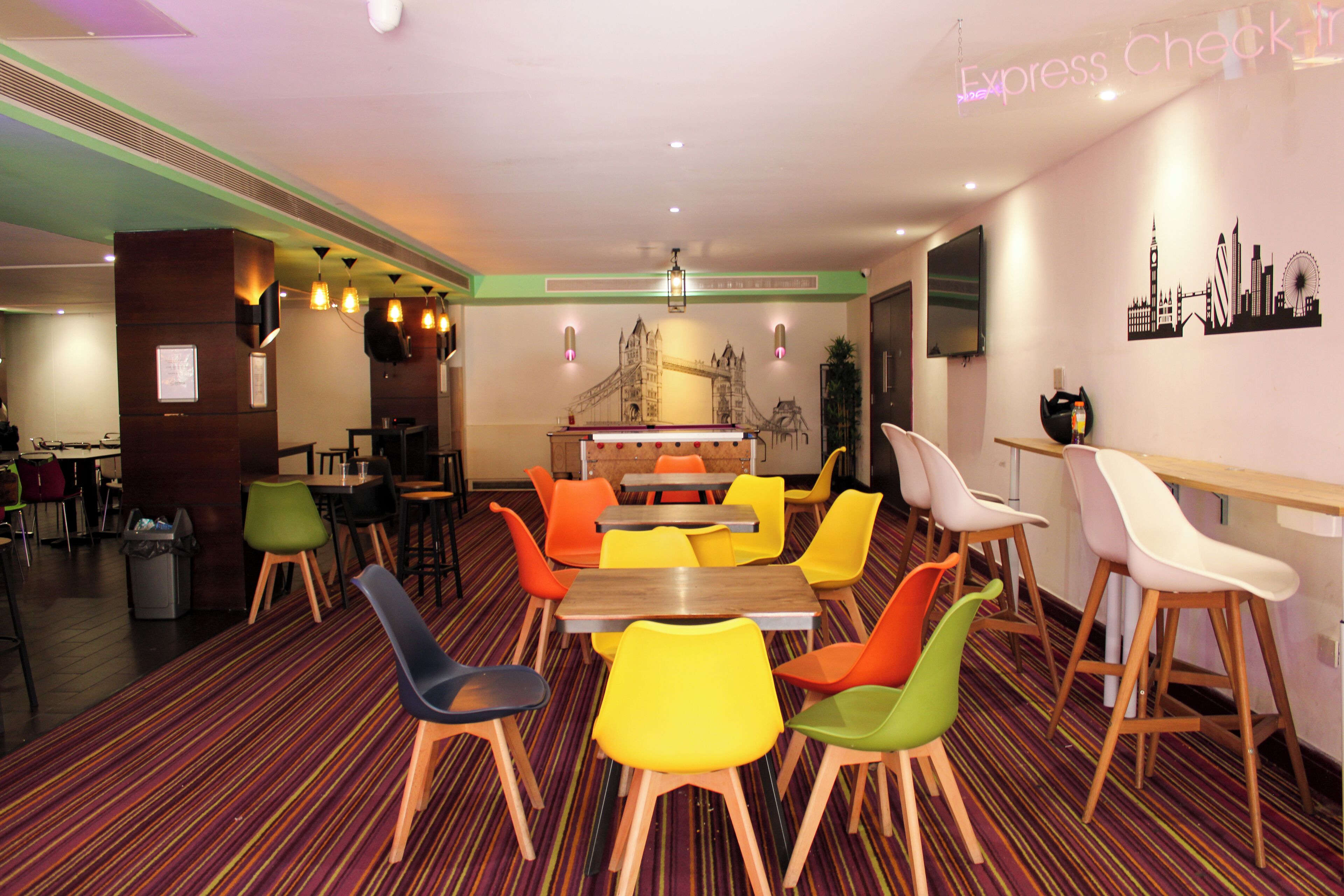 A dining area with colorful chairs and tables, a central island, and a mural of a famous bridge.