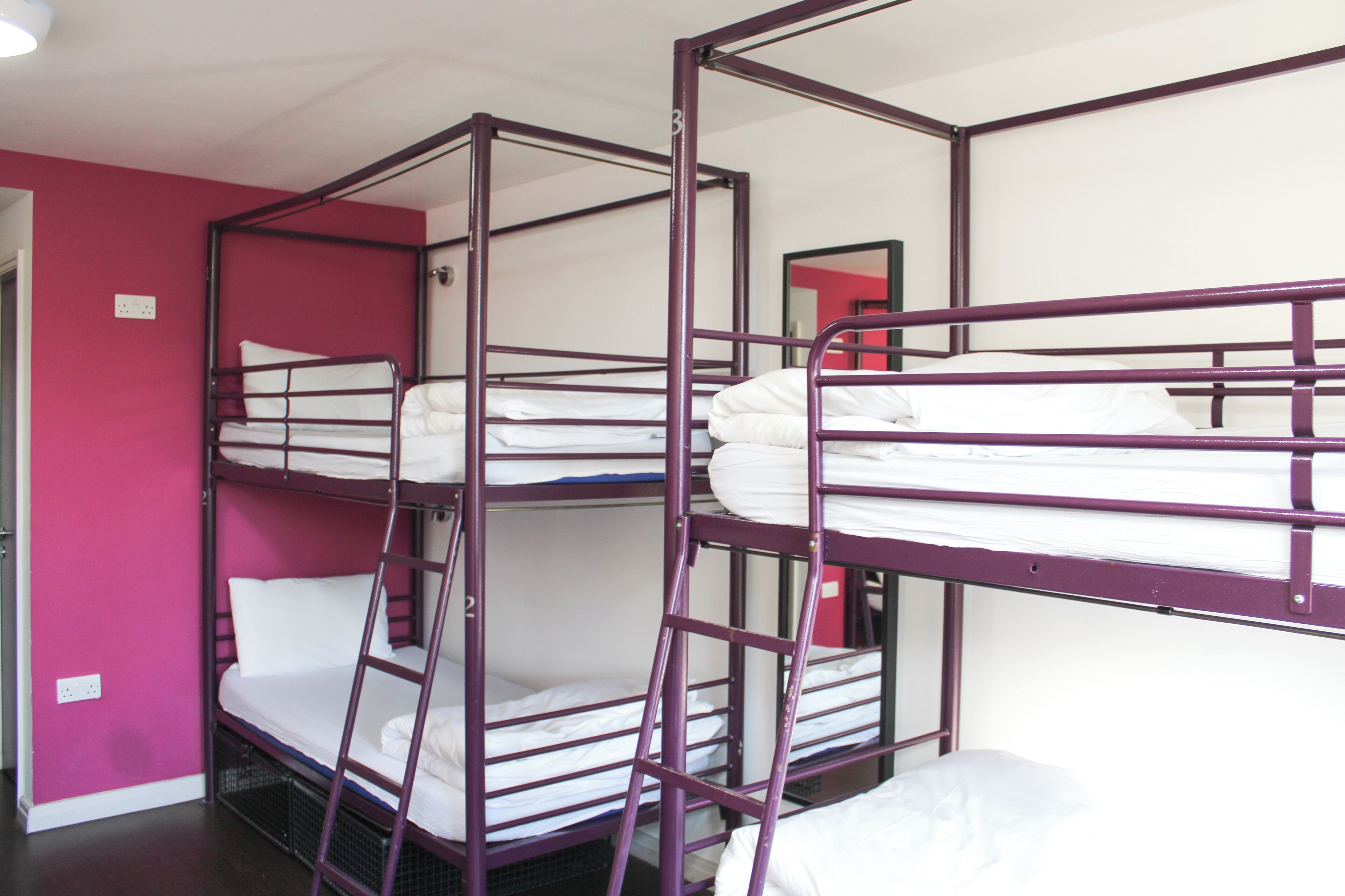 Camera con letto a castello a tre piani, ognuno con biancheria bianca e struttura in metallo viola.