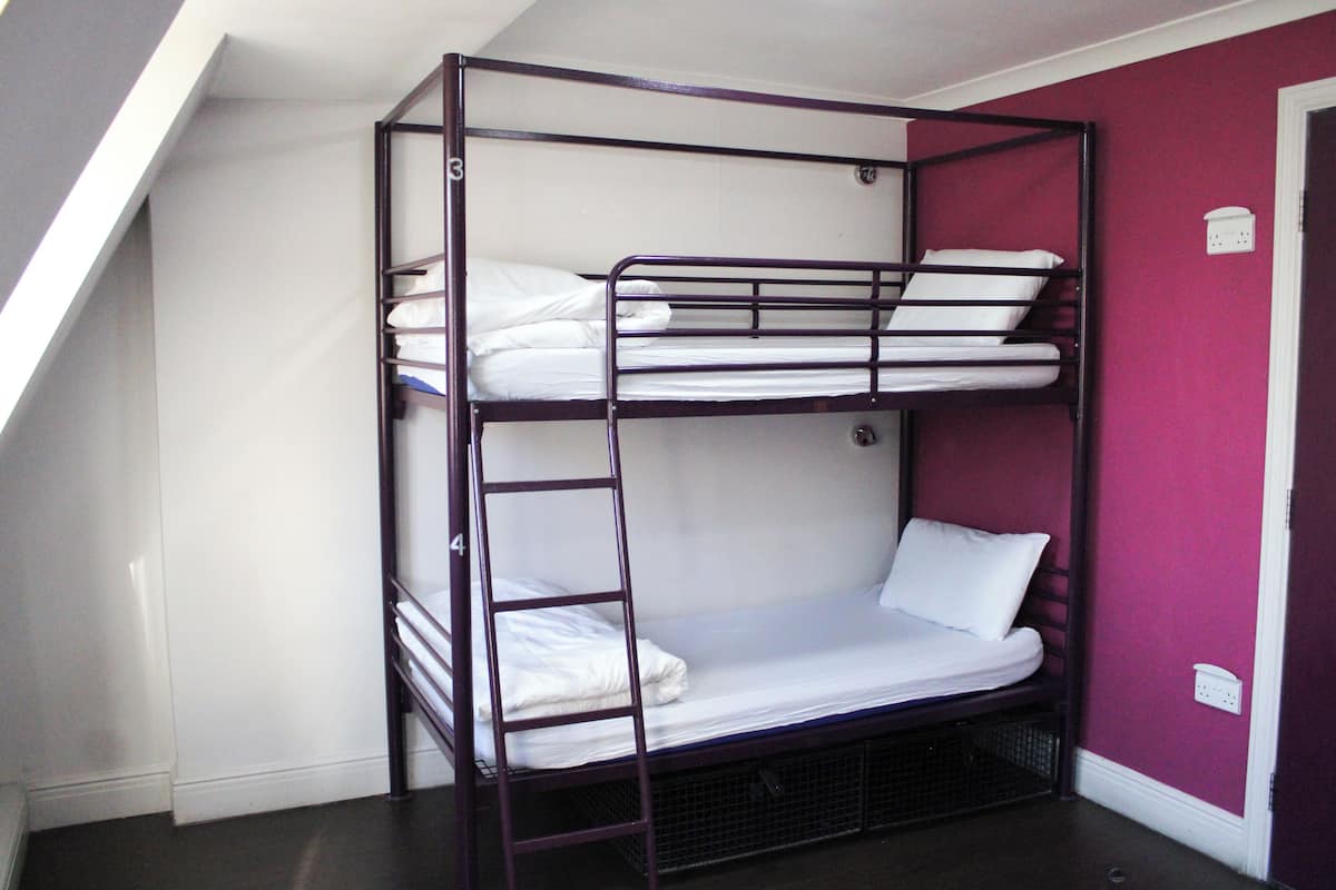 A bunk bed with a ladder, white bedding, and a purple wall.