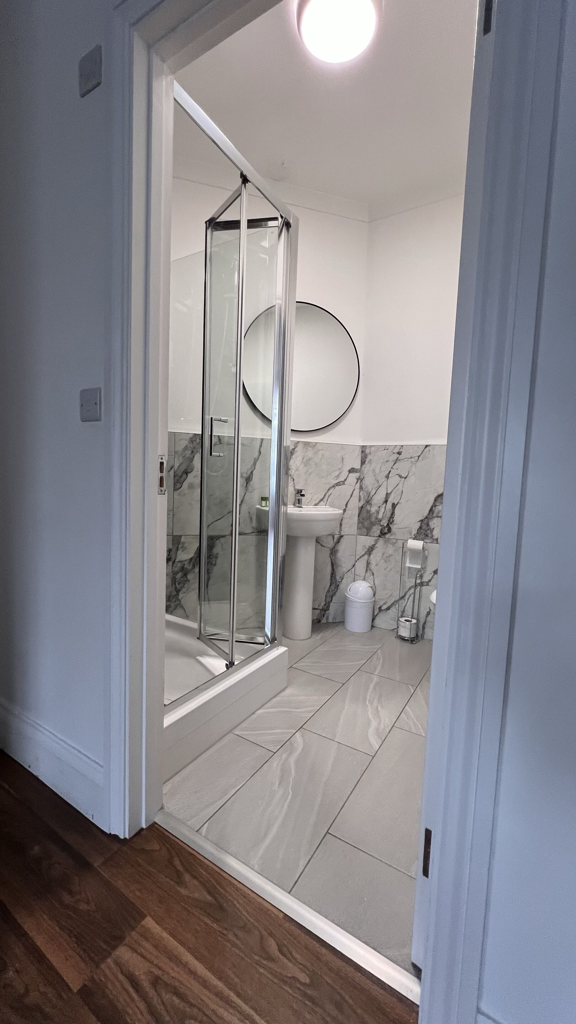 A modern bathroom with a glass shower enclosure, a sink, and marble-tiled walls.