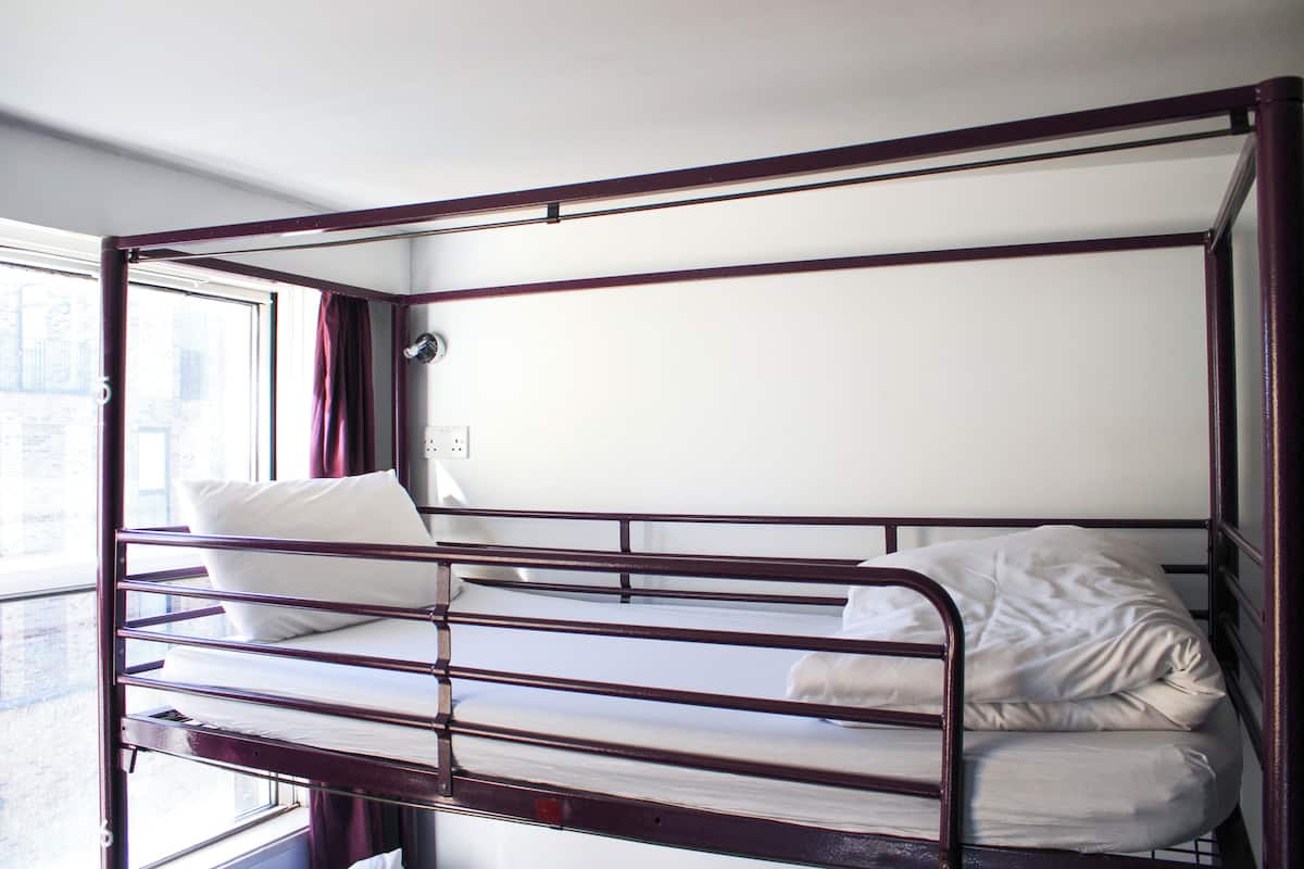 A bunk bed with a window, white bedding, and a metal frame.