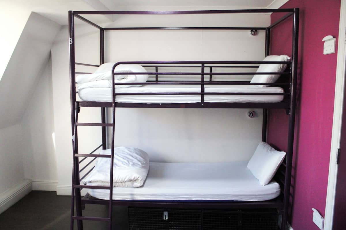 A bunk bed with white bedding in a room with a sloped ceiling and a purple wall.