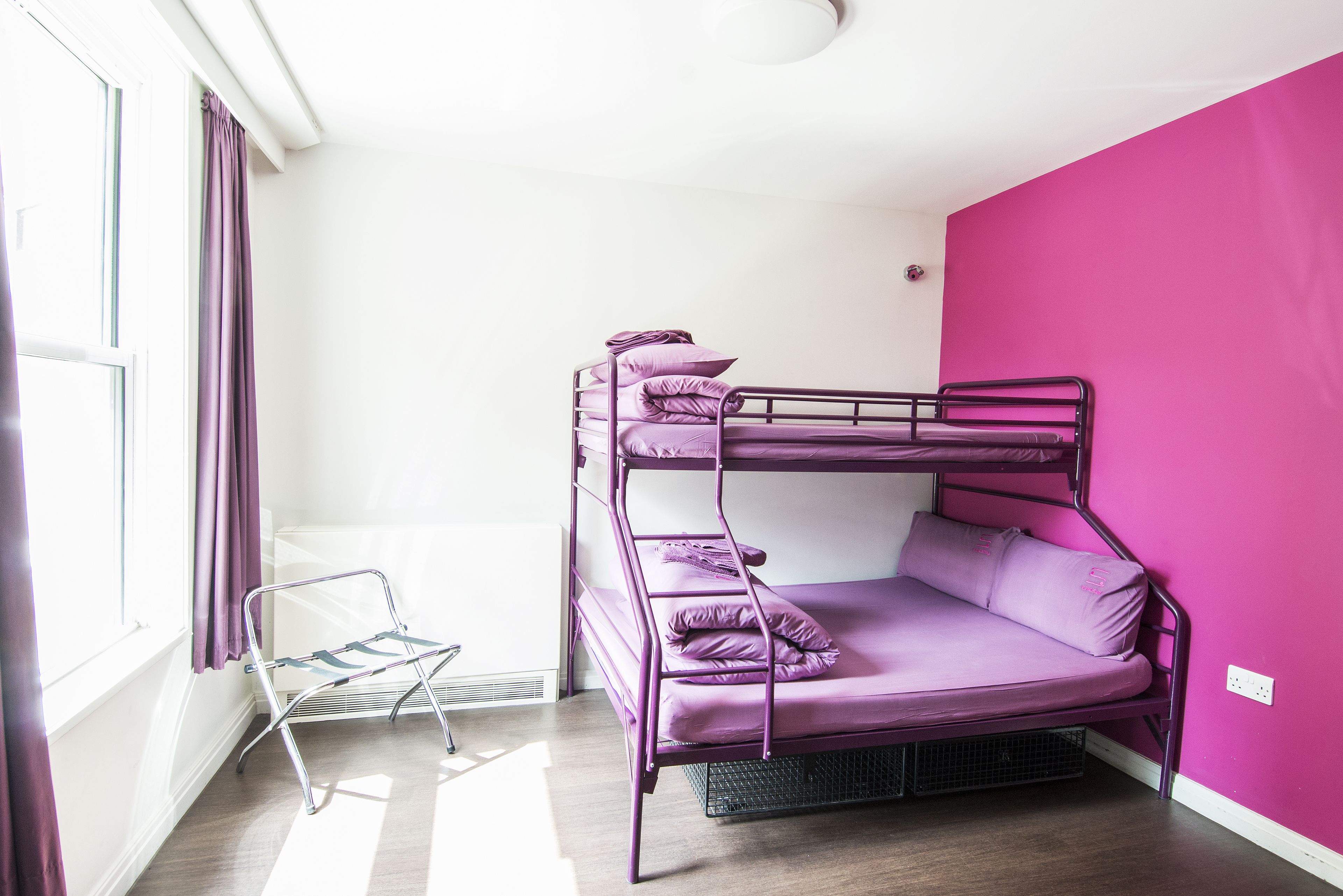 A bunk bed with purple bedding in a room with white walls and a pink accent wall.