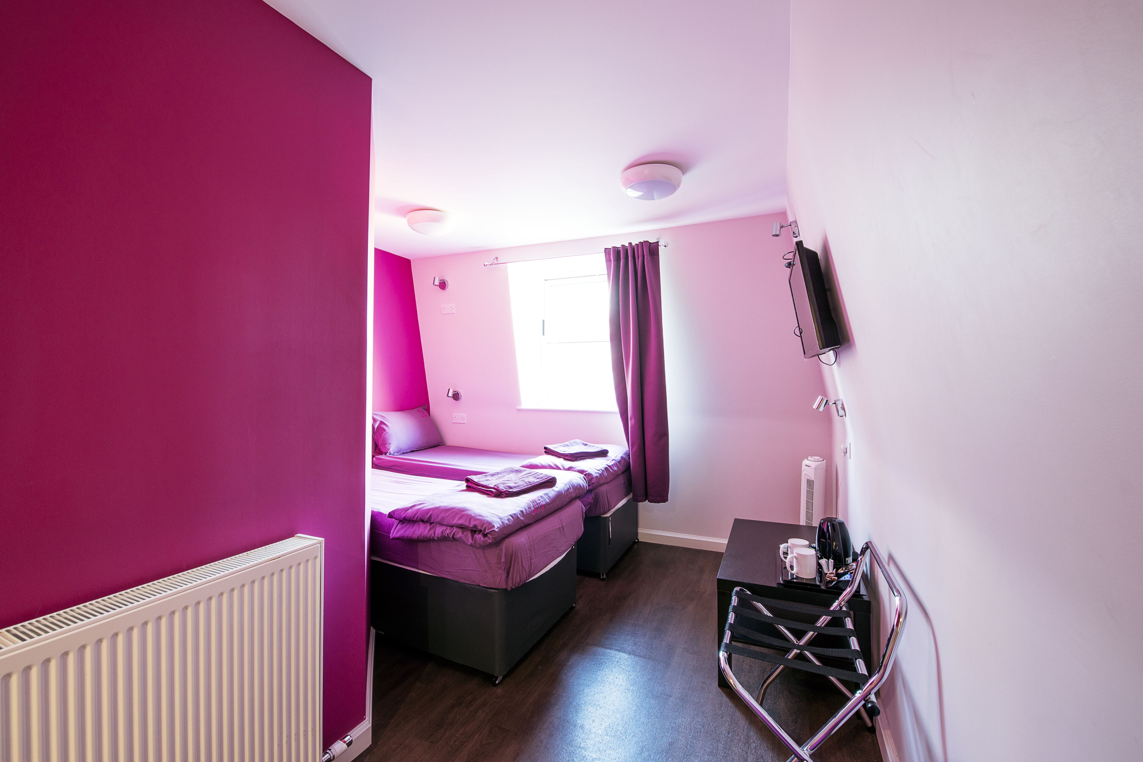 A room with a bed, a desk, a chair, a radiator, and a window with curtains.