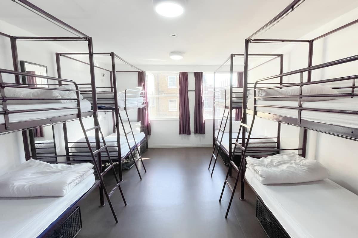 A dormitory room with bunk beds, a window with curtains, and a radiator.