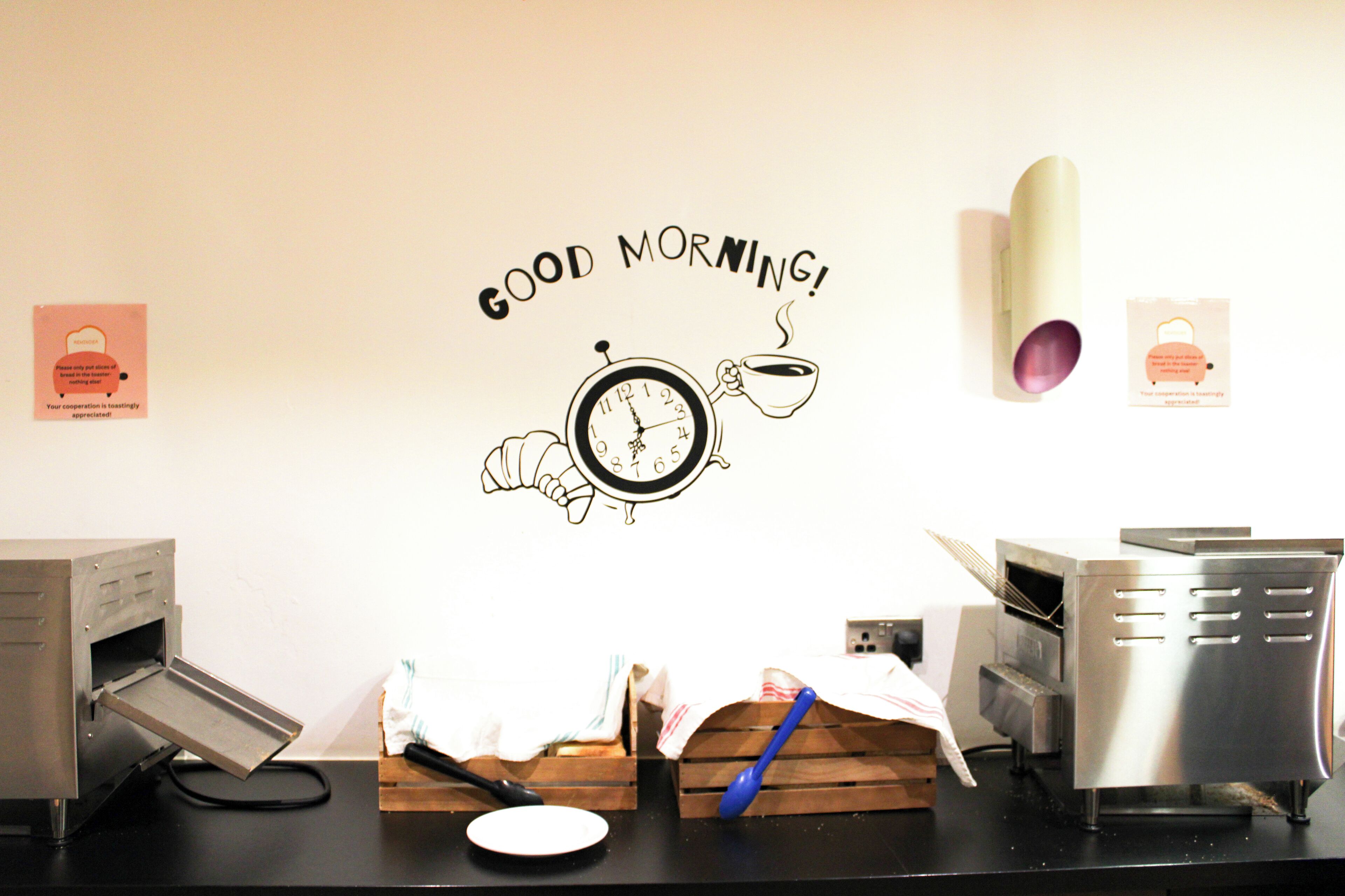 A kitchen counter with a coffee machine, a clock, and a wall with a 'Good Morning!' sign.