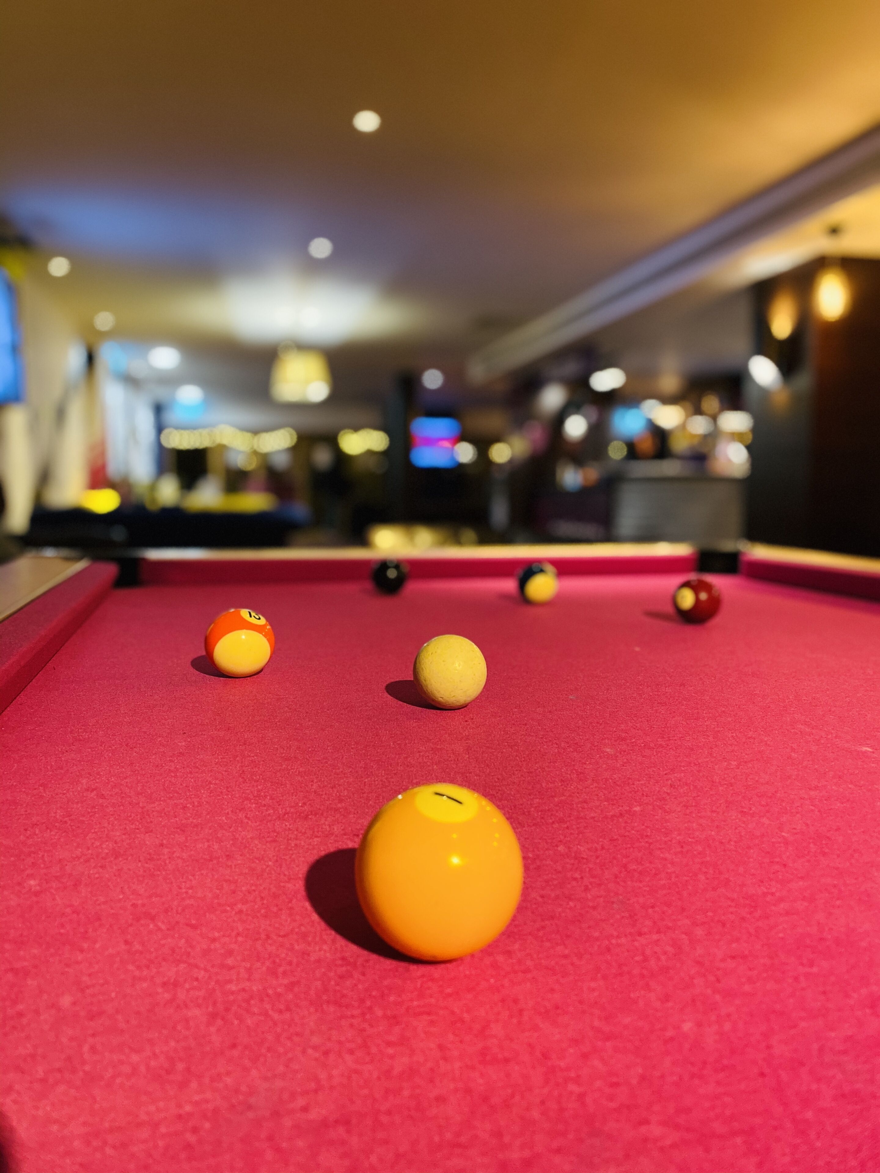 A pool table with balls in focus and a blurred background of a room with lights and a television.