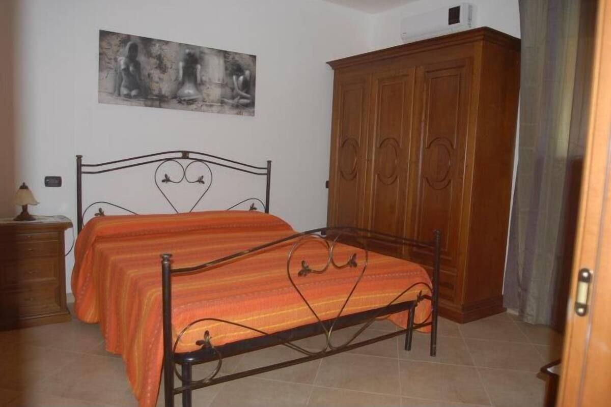 Une chambre à coucher avec un cadre de lit en métal, deux lits avec une literie à rayures, une armoire en bois et un tableau accroché au mur.