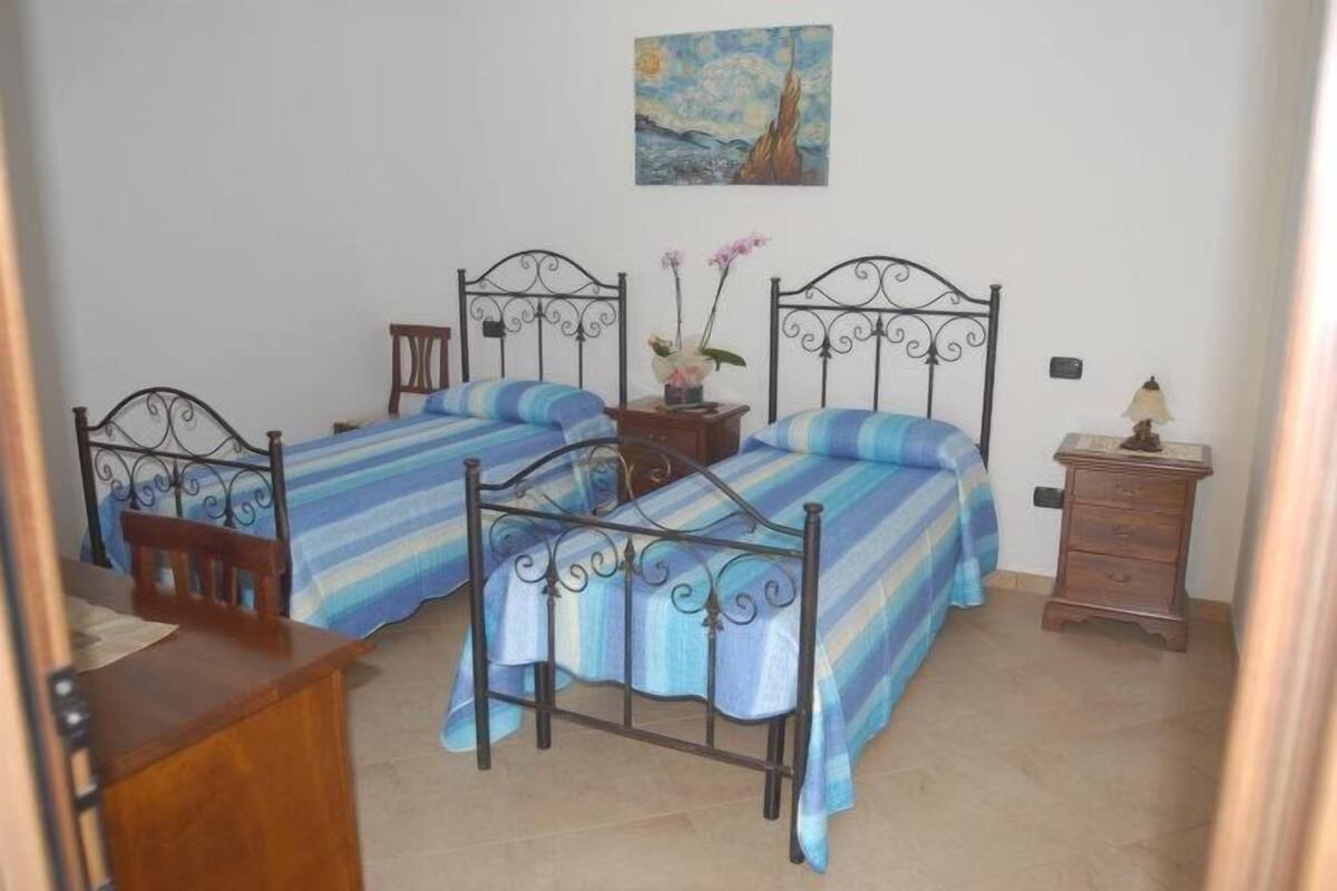 Une chambre avec deux lits, un bureau, une chaise, une table de chevet et un tableau au mur.